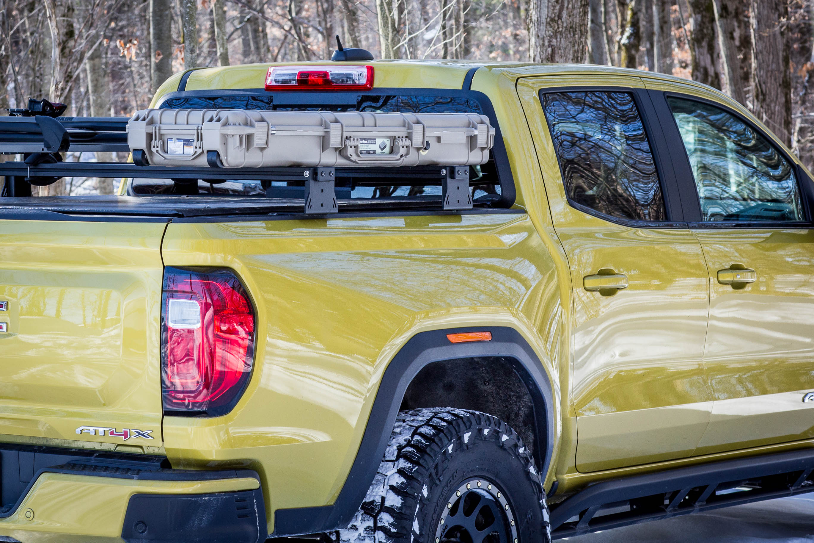 Yellow truck with a bed rack and off-road tires in a forest setting