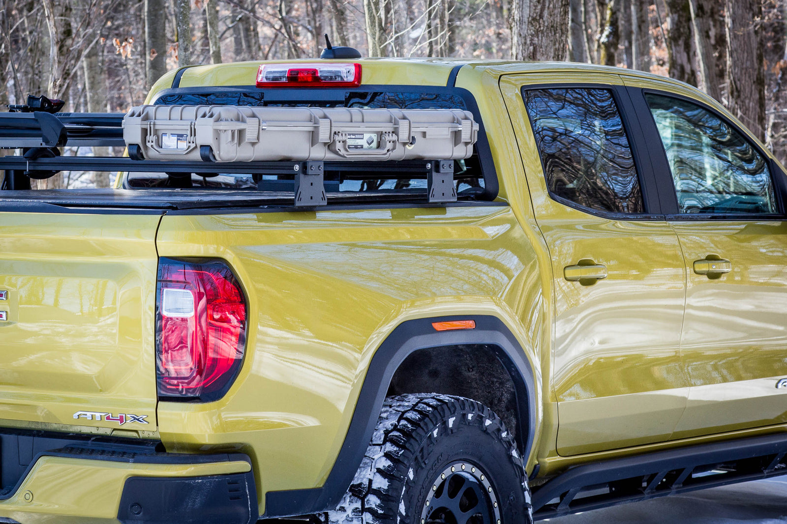 Yellow truck with a bed rack and off-road tires in a forest setting